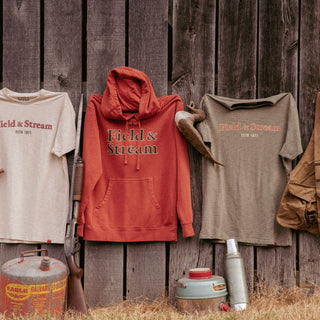 4 T-shirts hanging on a fence with hats below positioned on vintage gas can