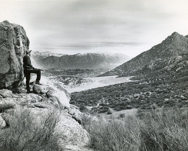 Man with rifle overlooking scenic view, mountains in the distance